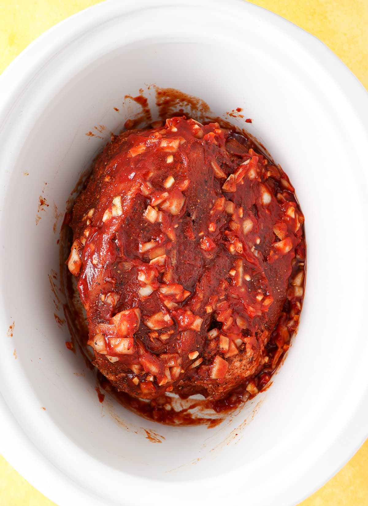A large pork shoulder that has been seasoned and placed in a crock pot ready to cook