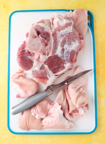 A pork shoulder on a cutting board with a meat knife that has trimmed off excess fat setting beside it