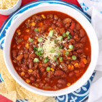 Homemade taco soup with cheese and diced green onions on top and some chips on the side