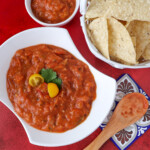 cherry tomato salsa with a spoon that scooped it into a small bowl next to chips