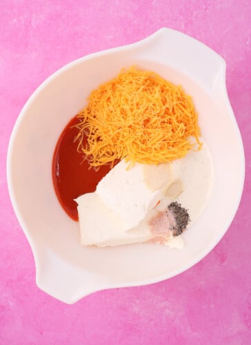 A bowl with cream cheese shredded yellow cheese buffalo sauce ranch dressing and seasoning ready to be Blended