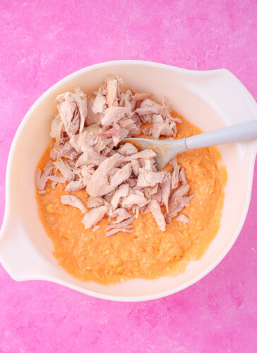Buffalo dip in a bowl with shredded chicken on top ready to be stirred in