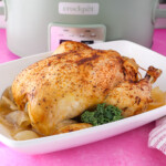 A whole chicken that has been cooked in the crock pot on a platter with roasted onions
