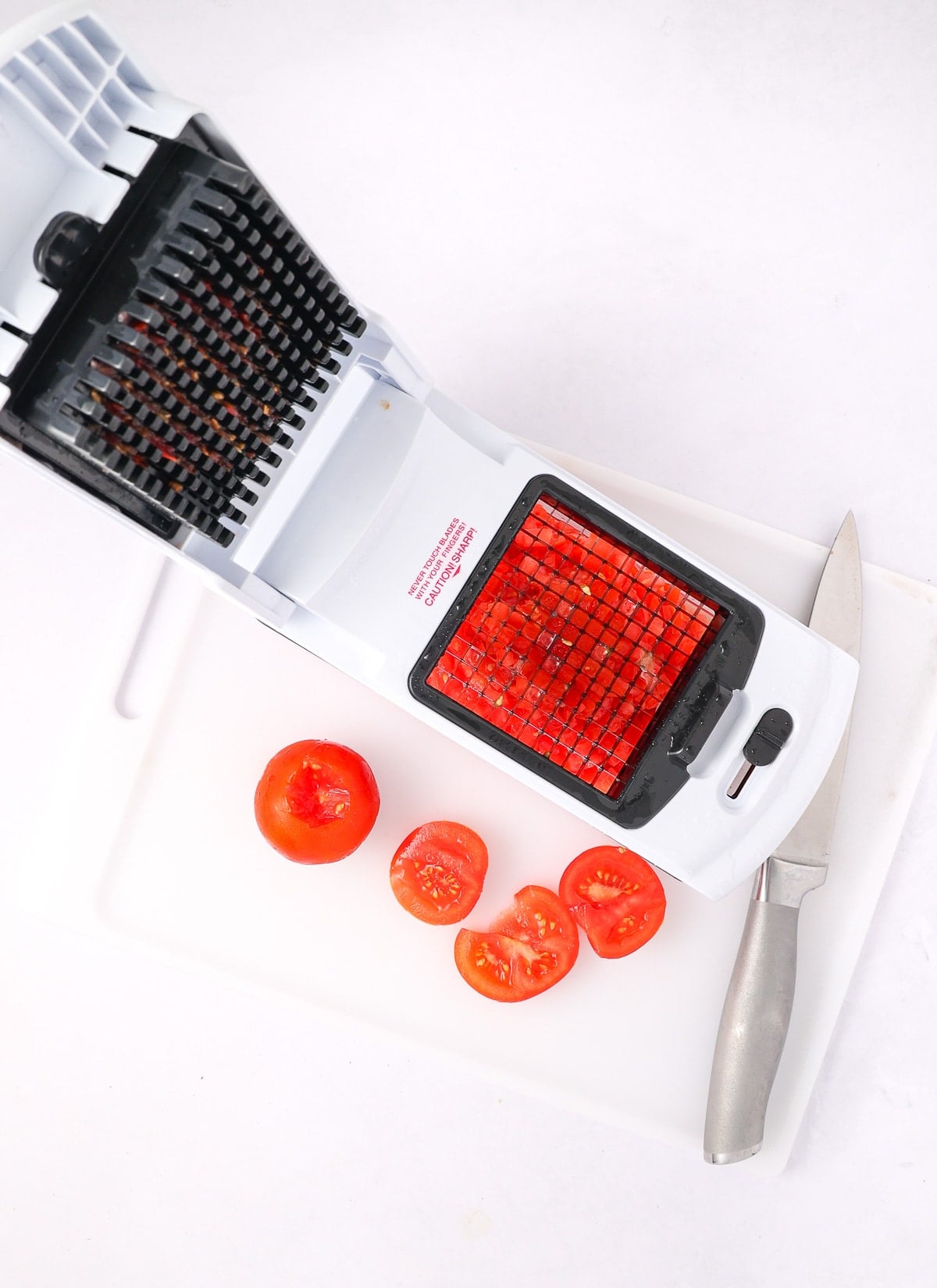 Tomatoes on a cutting board being chopped in a food chopper with a small blade