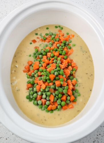 Creamy Crock-Pot chicken and dumplings ready to be cooked with frozen peas and carrots on top