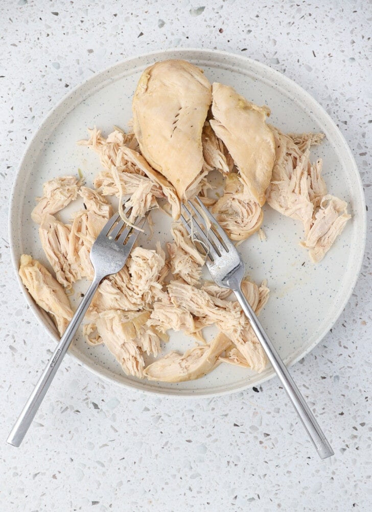Cooked chicken breast being shredded with forks