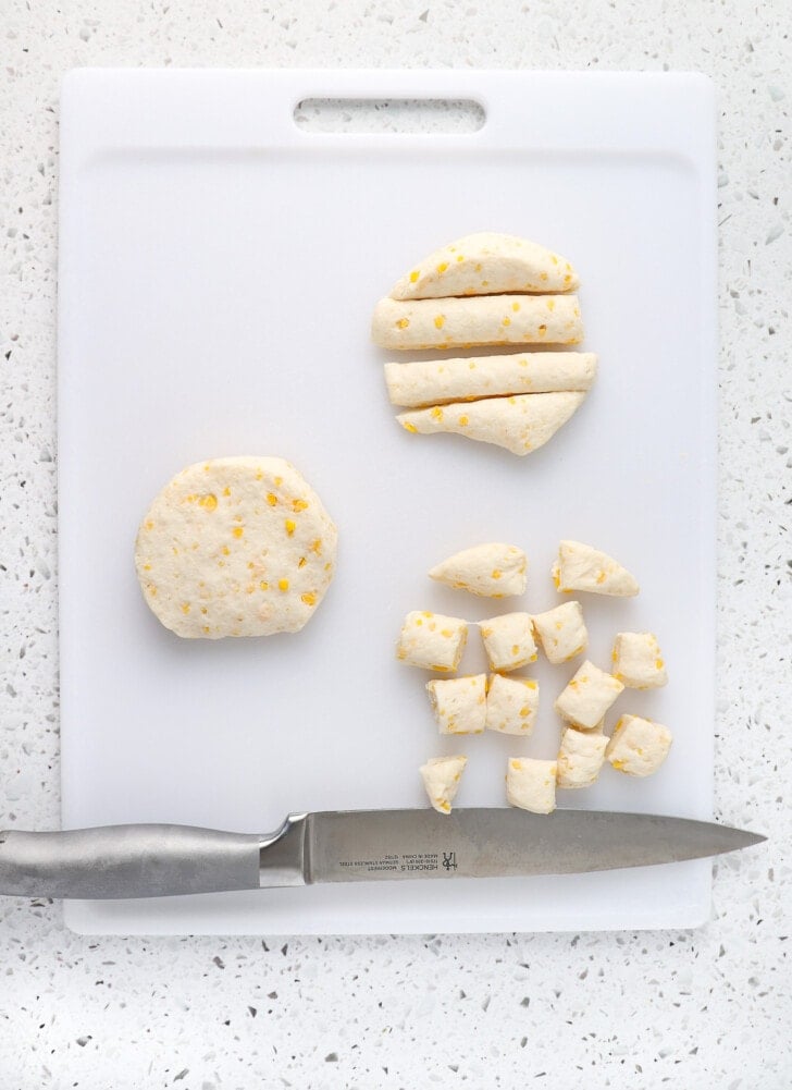 Biscuit dough on a cutting board with a long knife cutting them into squares