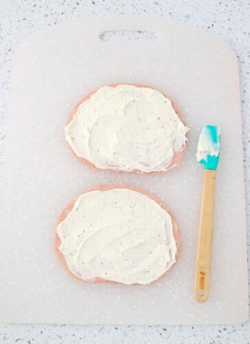 Ham slices covered in cream cheese with a spatula