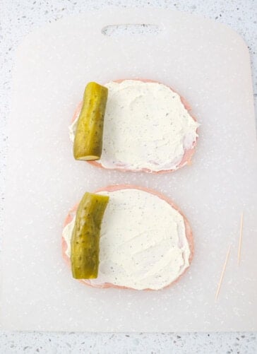 Piece of ham with cream cheese spread on it and a pickle on the edge