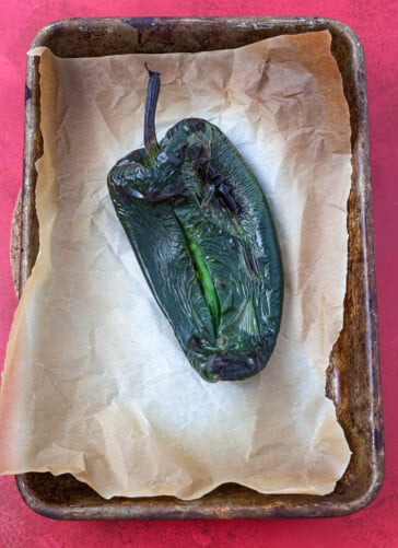 Roasted poblano pepper that has been charred sitting on a cookie sheet