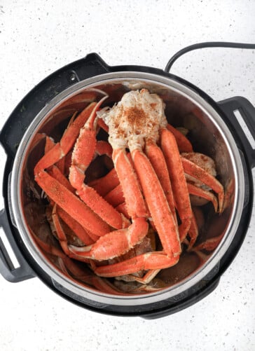Crab legs going into an instant pot sprinkled with Old Bay