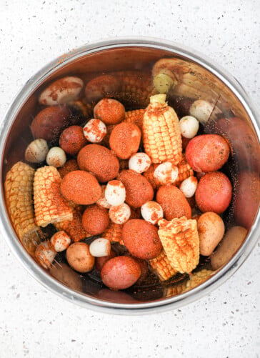 The vegetables being put in an instant pot for Low Country Boil including potatoes corn onions sprinkled with Old Bay