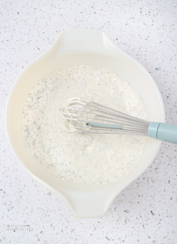 Creamy dill dip being mixed in a bowl with a whisk