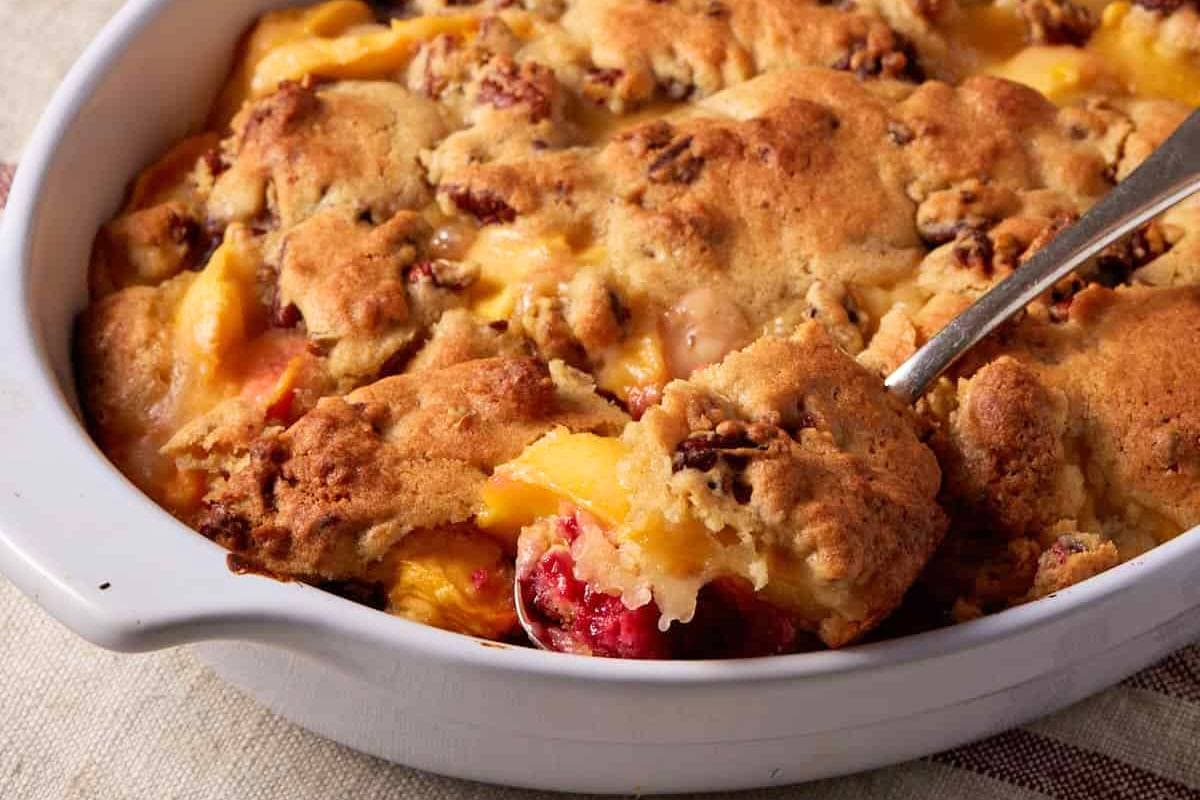 Peach cobbler being dished out of a baking dish