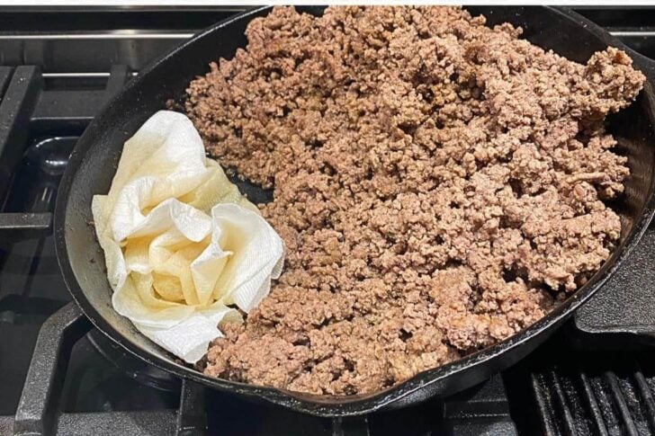 Ground beef being cooked in a black Skillet and then using paper towel to soak up the excess oil