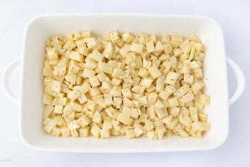 A white rectangular baking dish filled with evenly diced potatoes seasoned with pepper and herbs, ready to be cooked.