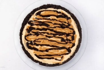 A pie in a clear dish with a dark chocolate crust. The creamy filling is topped with drizzles of chocolate and peanut butter, creating a swirled pattern. The background is a plain white surface.