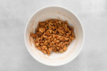 A white bowl filled with roasted cashews on a light gray surface.