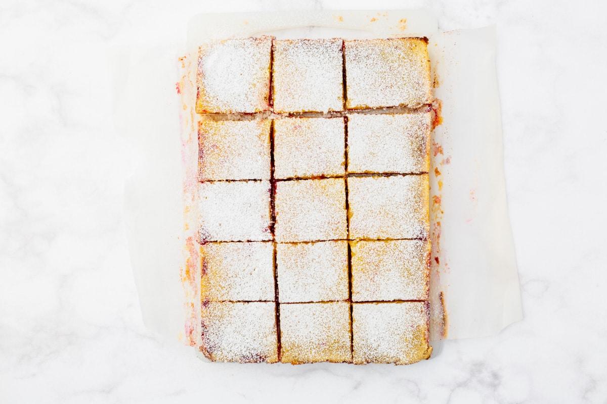 A tray of square-cut pastries dusted with powdered sugar, arranged neatly on parchment paper against a marble surface.