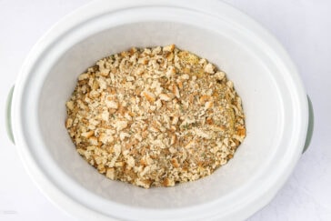A white slow cooker filled with seasoned bread crumbs on a light background.