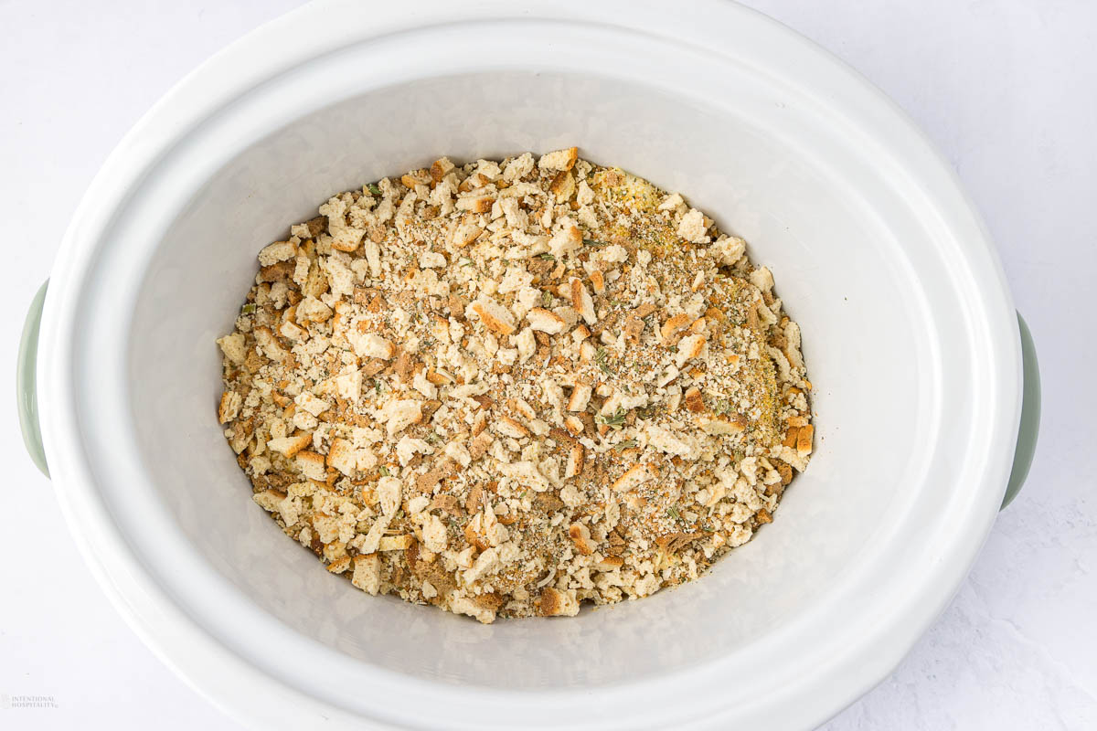 A white slow cooker filled with seasoned bread crumbs on a light background.