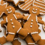 A pile of decorated gingerbread cookies featuring smiling gingerbread people with white icing details, alongside star and round-shaped cookies in the background.