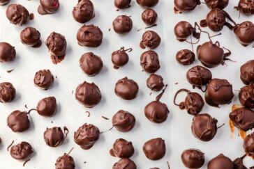 A tray lined with parchment paper covered in various sizes of chocolate-coated truffles. The truffles, scattered randomly, have a smooth and glossy finish with some chocolate drips and swirls decorating the surface.
