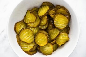 A white bowl filled with crinkle-cut pickle slices on a marble surface.