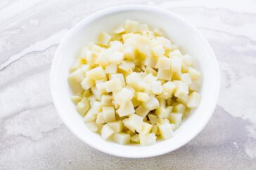 A white bowl filled with small, neatly diced potato cubes placed on a light, textured surface.
