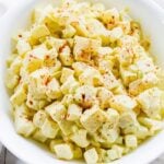 A bowl filled with creamy potato salad, featuring diced potatoes and a sprinkling of paprika on top, creating a colorful and appetizing dish.