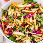 A vibrant salad featuring thinly sliced red and green apples, shredded red cabbage, carrots, and leafy greens, all mixed in a white bowl.