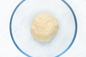 Round ball of dough in a clear glass bowl on a white surface.
