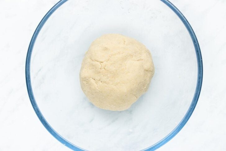 Round ball of dough in a clear glass bowl on a white surface.
