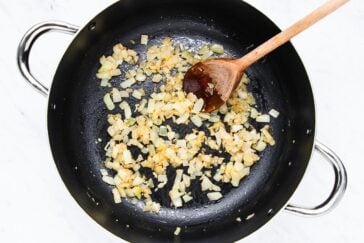 Chopped onions are being sautéed in a black pan with a wooden spoon.
