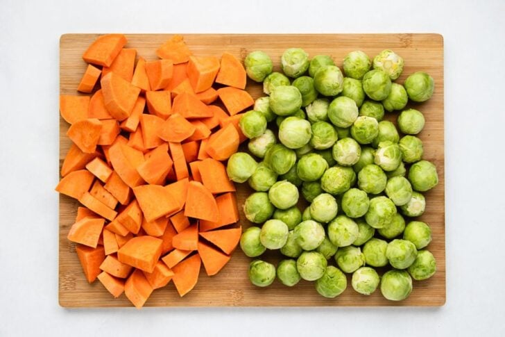 Chopped sweet potatoes and whole Brussels sprouts arranged side by side on a wooden cutting board.