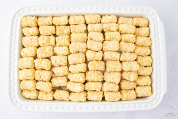A white rectangular baking dish filled with neatly arranged tater tots. The tots are golden brown and evenly distributed in rows, covering the bottom of the dish completely.