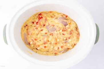 Slow cooker filled with a creamy mixture of chopped red peppers, onions, and chicken, ready to be cooked.