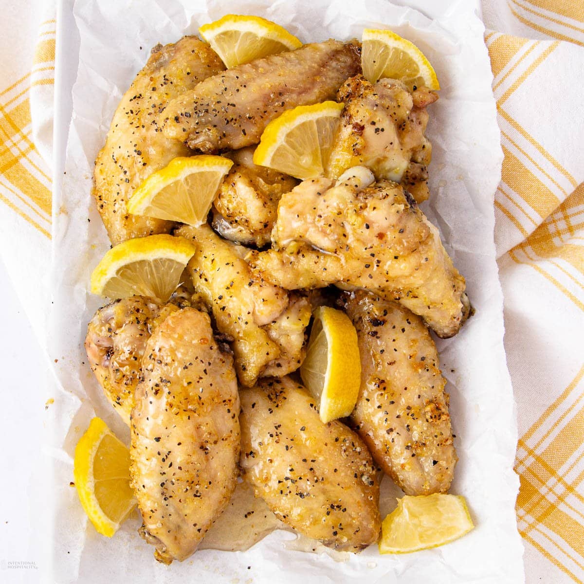 Honey-glazed lemon pepper wings with fresh lemon wedges on a white plate.