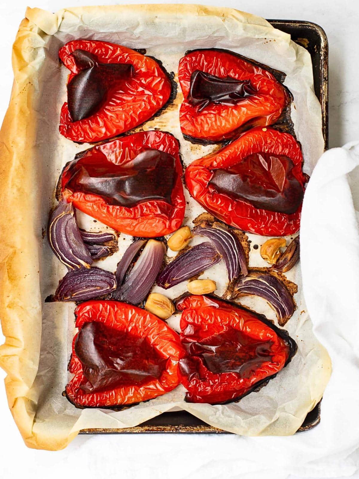 Roasted red bell peppers, purple onion wedges, and whole garlic cloves on a parchment-lined baking sheet bring a hint of modern cowboy candy flair. The vegetables are charred and arranged in a rustic manner.
