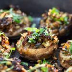Close-up of stuffed mushrooms topped with chopped herbs. The mushrooms are filled with a mixture of vegetables and garnished with green herbs for a fresh look. The background is slightly out of focus, highlighting the texture of the filling.