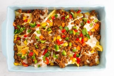 A casserole dish filled with nachos topped with seasoned ground beef, melted cheese, and diced red, green, and yellow bell peppers.