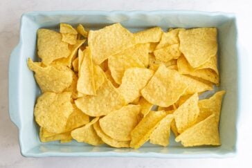 A light blue rectangular dish filled with yellow corn tortilla chips, spread out in an even layer on a white surface.