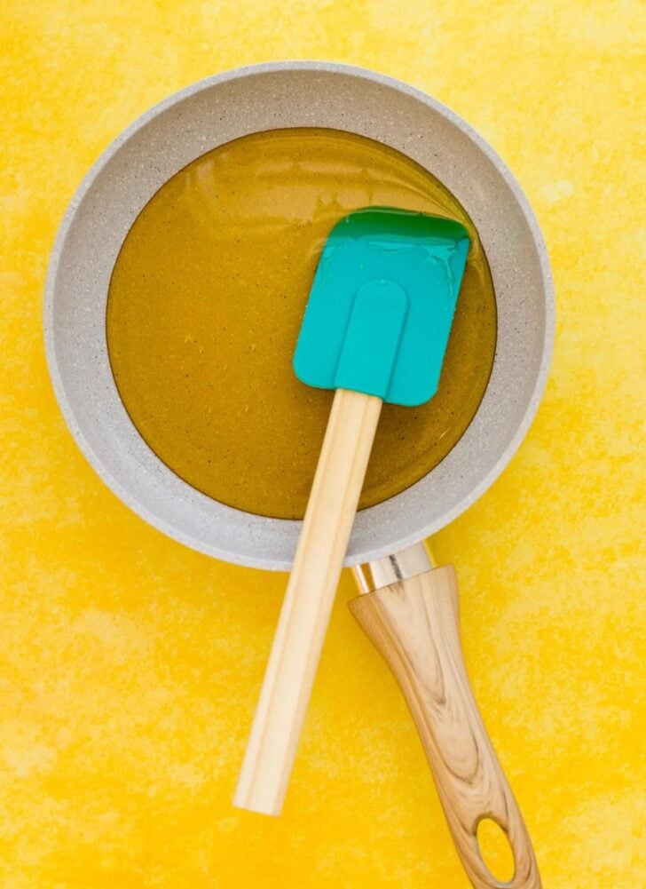 A frying pan filled with oil and a green silicone spatula resting inside—perfect tools for starting your canned cowboy candy recipe—all placed on a bright yellow surface.