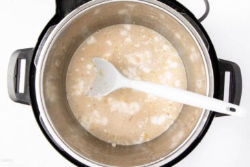 An overhead view of an Instant Pot containing a mixture of liquid and chunks, being stirred with a white spoon.