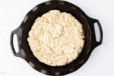 Unbaked biscuit dough spread evenly in a black cast iron skillet, photographed from above on a white background.