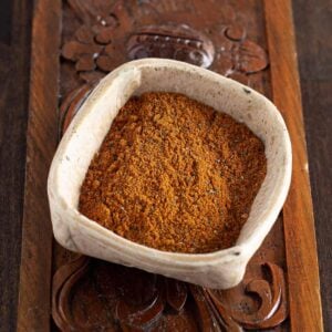 A small, square, white bowl filled with reddish-brown spice powder sits on a carved wooden surface—perfect to add a kick to your favorite canned cowboy candy recipe.