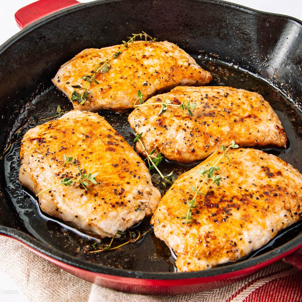 Four seasoned and seared chicken breasts cooking in a black cast iron skillet.