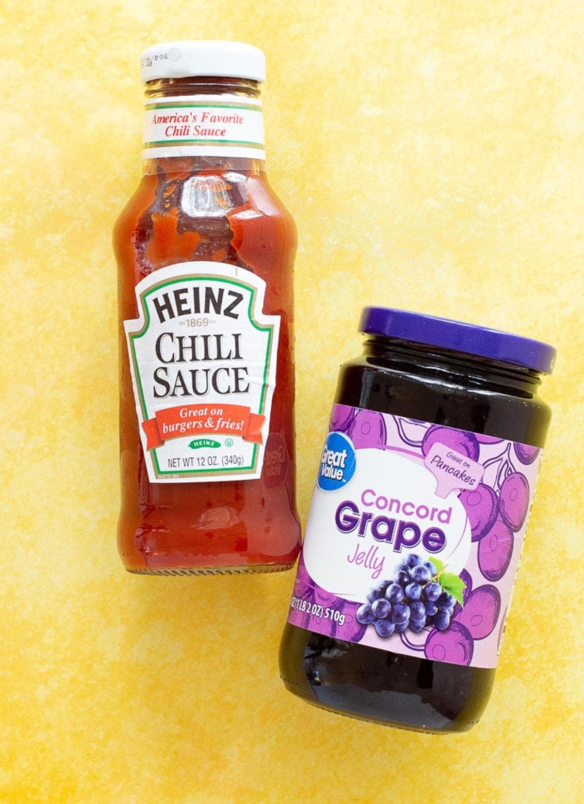 A bottle of Heinz Chili Sauce and a jar of Great Value Concord Grape Jelly sit on a yellow surface, perfect ingredients for a classic canned cowboy candy recipe.