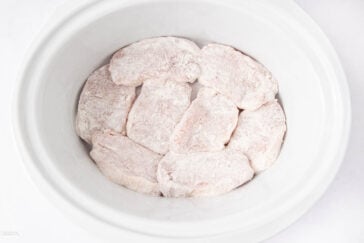 Raw, flour-dusted pork chops arranged in a single layer inside a white slow cooker, ready for cooking.