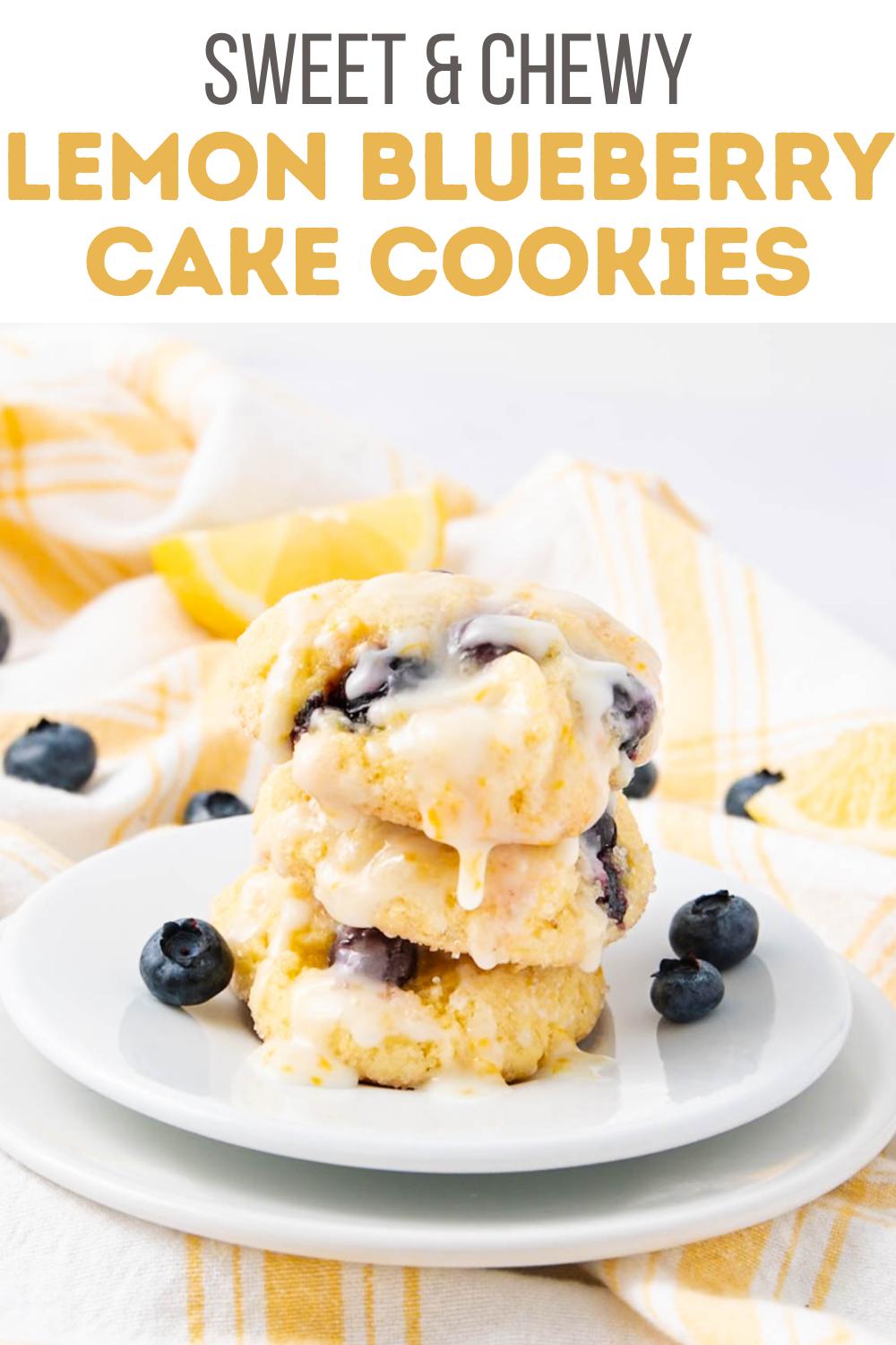 Three lemon blueberry cookies stacked on a white plate, drizzled with icing and surrounded by fresh blueberries. A yellow and white striped towel and a lemon wedge are in the background. Text above reads: "Sweet & Chewy Lemon Blueberry Cake Cookies.